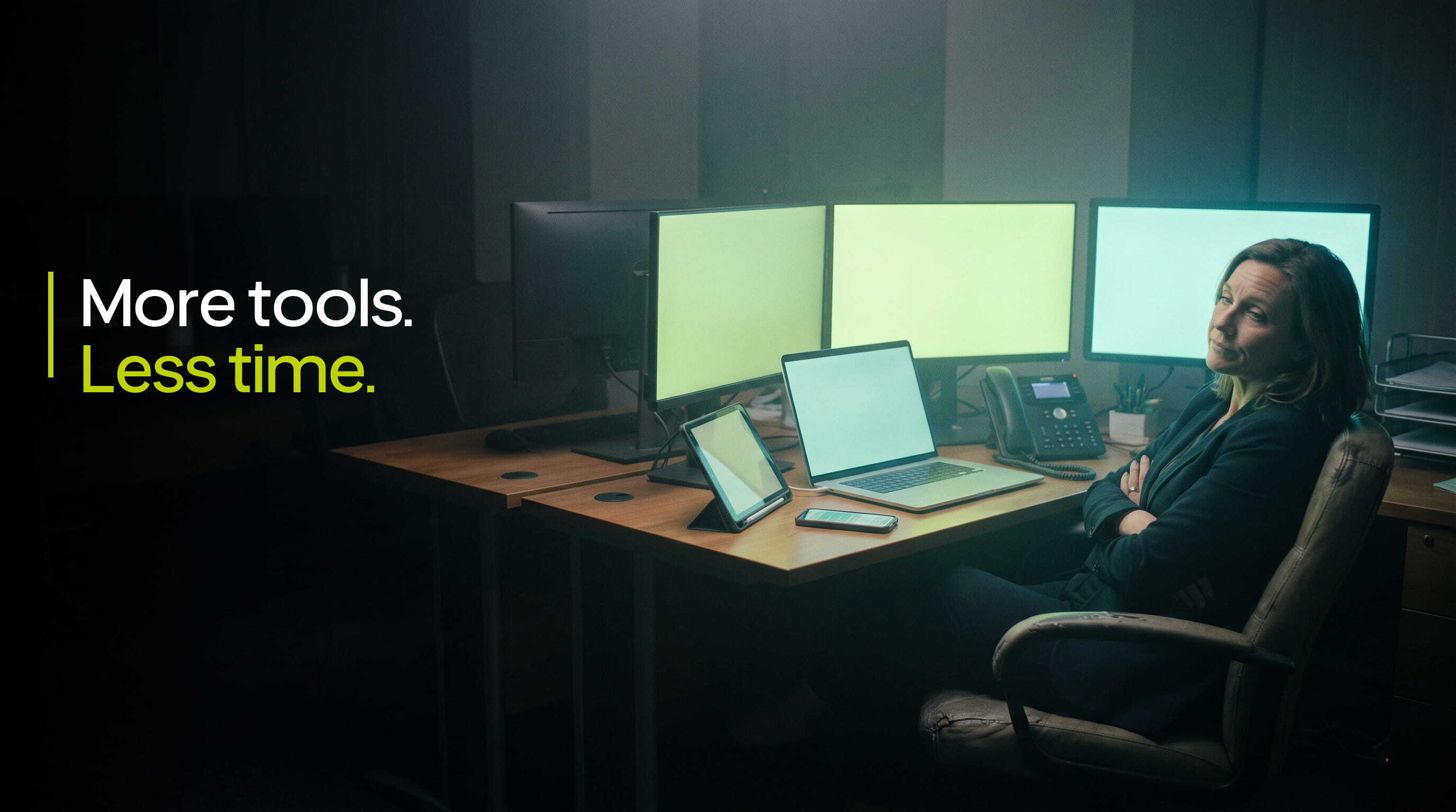 Insurance agency owner sitting back at a desk surrounded by monitors, laptop, tablet and phones, illustrating agency software overload